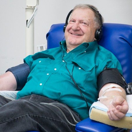 Person wearing headphones sitting in cot donating platelets and smiling.
