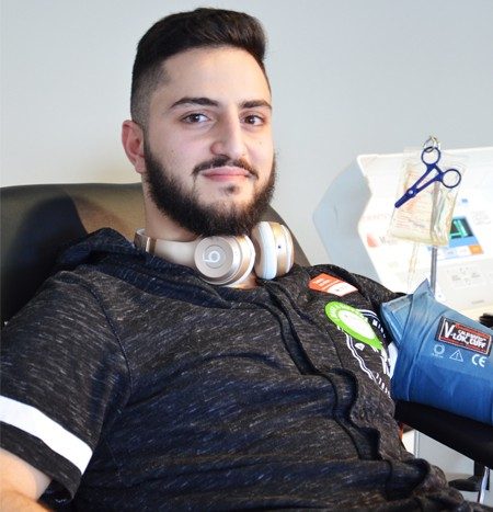 Person with headphones around back of neck sitting in cot donating plasma and smiling.