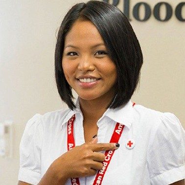 Person pointing at Red Cross pin on their shirt.